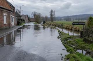 Rue partiellement inondée à Flines-lez-Mortagne ; maisons en briques, eau claire sur la chaussée près d’un canal, ciel nuageux, ambiance calme et hivernale.
