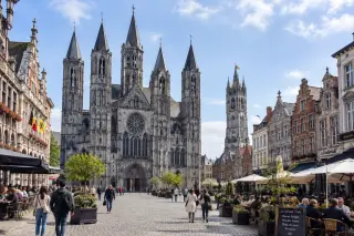 Notre-Dame Cathedral with five towers and the Grand-Place in Tournai, old facades, a few people walking and sitting at café terraces under soft natural light.